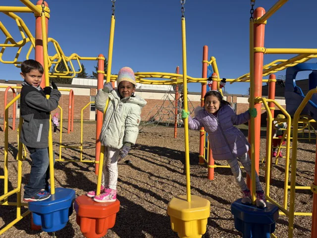Three FES students playing on colorful playground equipment